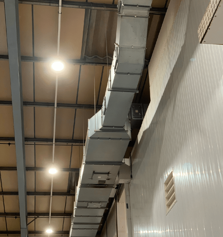 Dust-covered rectangular ductwork running above a tiled factory wall