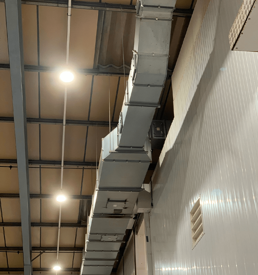 Dust-covered rectangular ductwork running above a tiled factory wall